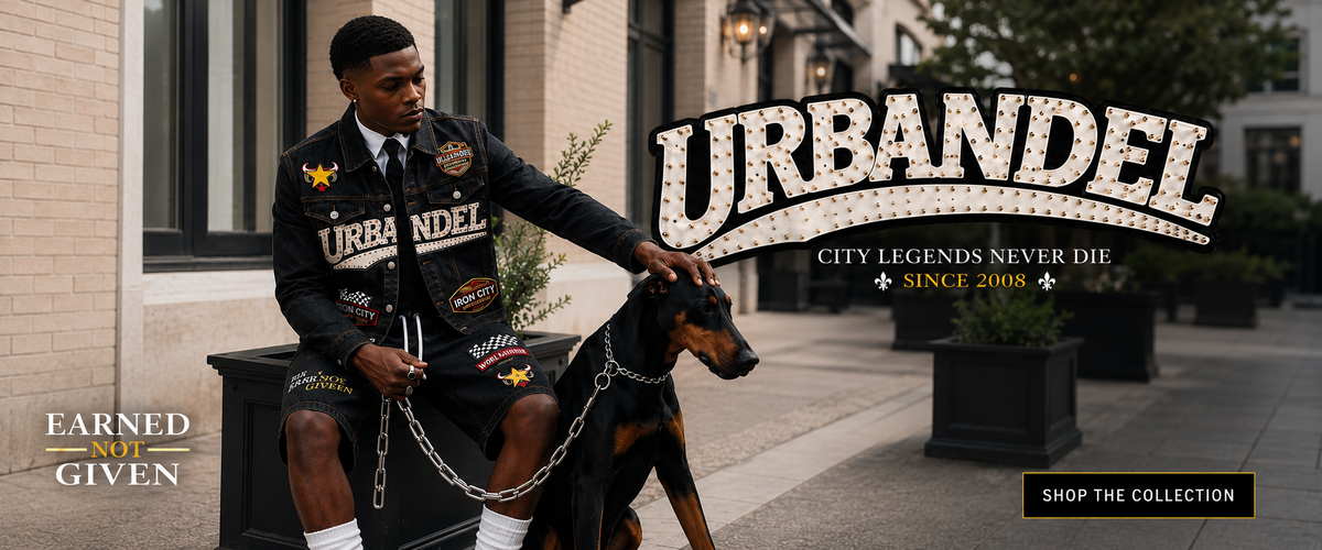 A man wearing a black Urbanel patch-covered jacket and shorts sits on a black bench next to a Doberman dog in an outdoor urban setting. Large 'URBANEL' text and promotional banners are overlaid on the image.