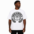 A man wearing a white short-sleeve t-shirt with a large black circular graphic on the chest featuring the word 'URBANDEL' and a winged emblem, photographed against a plain white background.